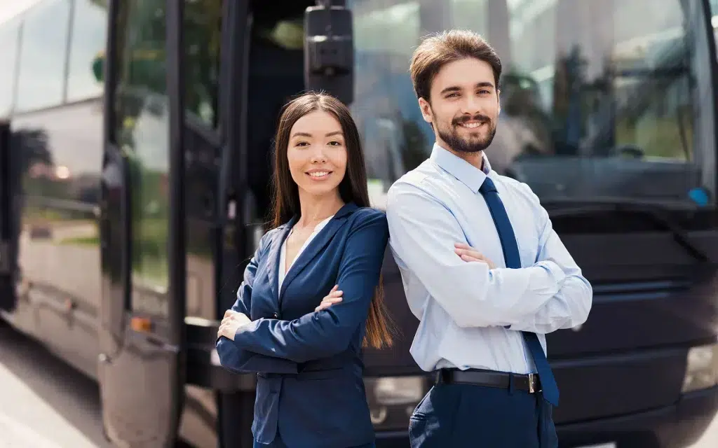 A young asian lady and a young man in front of a luxury bus hosting vip guests.