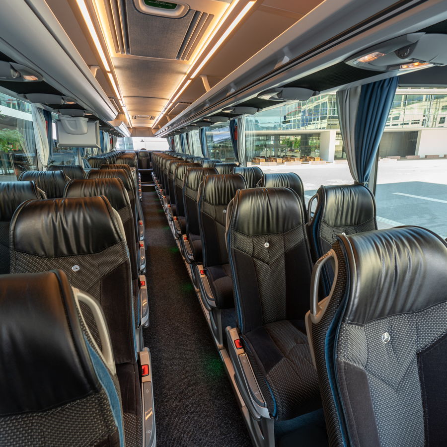 Innenansicht eines First Class Reisebus mit bequemen schwarzen Ledersitzen, stilvoller Beleuchtung und viel Komfort.