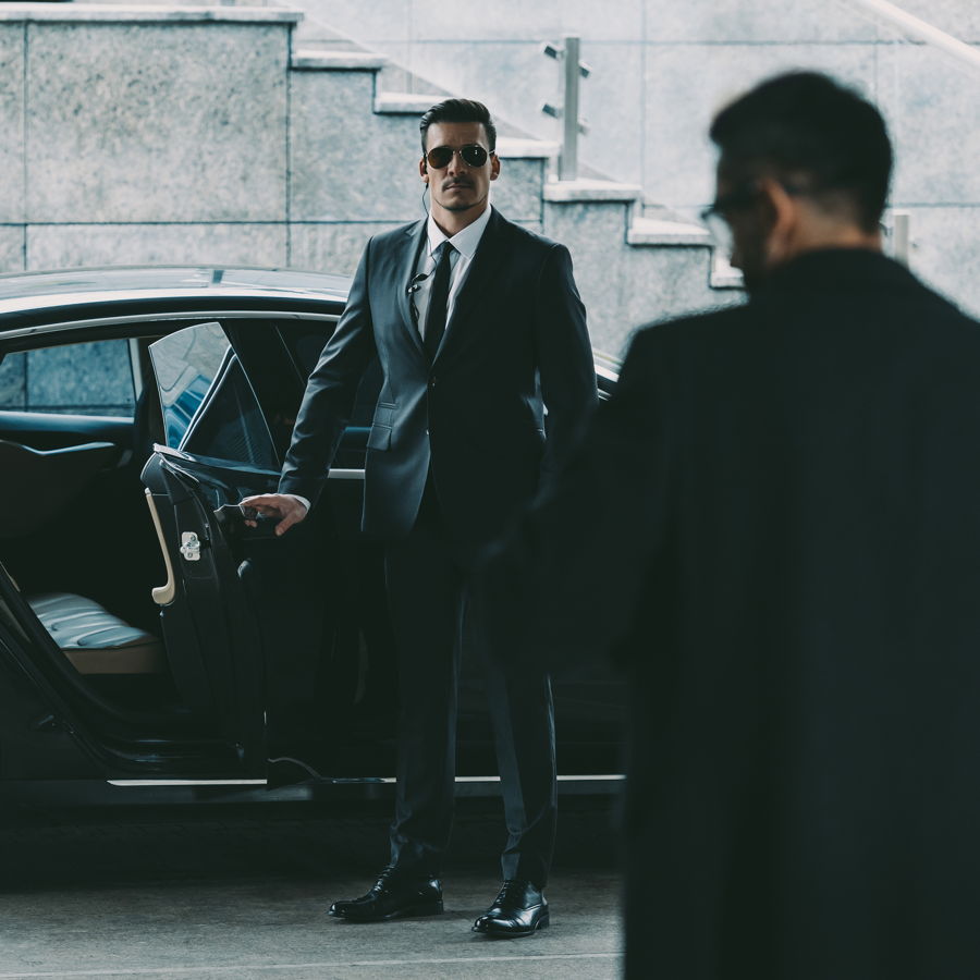 A security employee opens the door of a limousine for a VIP passenger and ensures the passenger's safety.