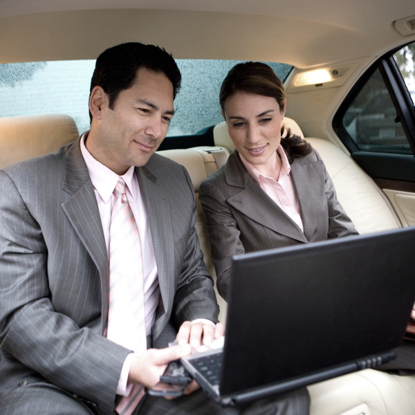 geschaeftstermin Eine Geschäftsmann und eine Geschäftsfrau arbeiten entspannt im Fond einer Limousine, während ein Chauffeur sie fährt.